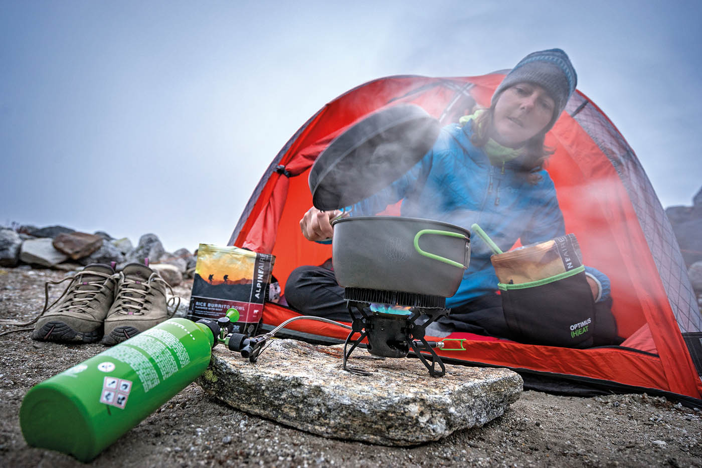A woman sits inside her tent using her camp stove to boil water for a dehydrated / freeze dried meal.